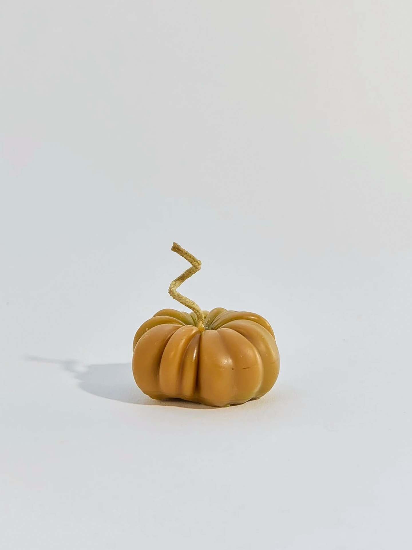A small Green Heirloom Tomato Candle with a unique tomato shape sits on a plain white surface.