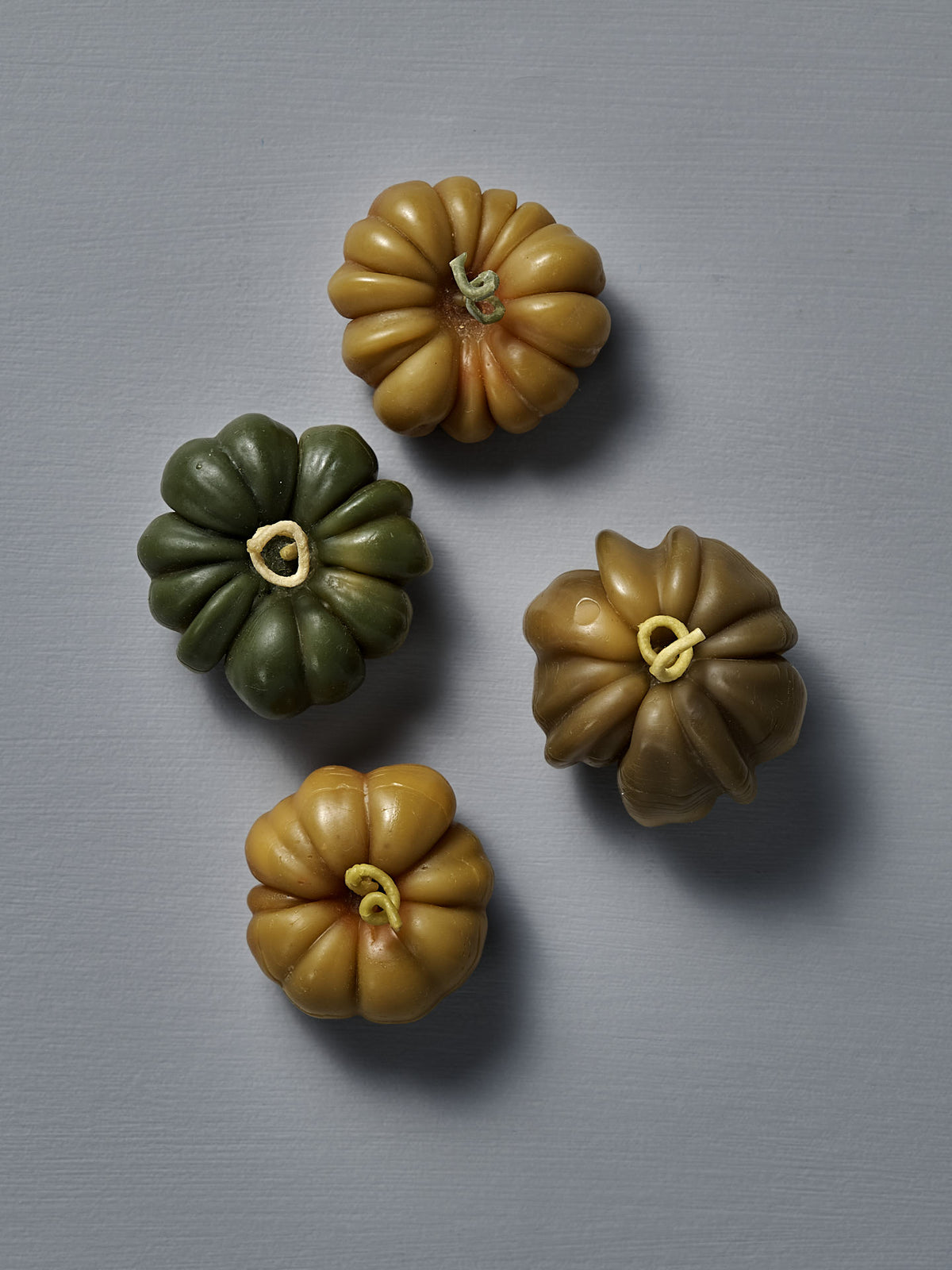 A small Green Heirloom Tomato Candle, with a ridged green and yellow surface, sits on a plain gray background—its unique charm inspired by New Zealand makes it perfect to display beside your favorite handmade décor.