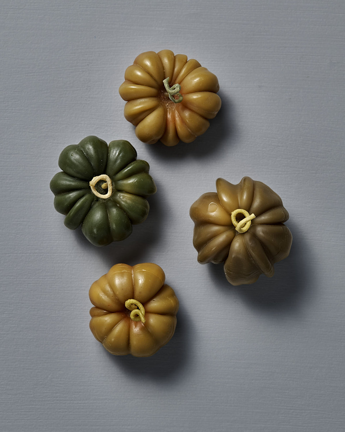 A small Green Heirloom Tomato Candle, with a ridged green and yellow surface, sits on a plain gray background—its unique charm inspired by New Zealand makes it perfect to display beside your favorite handmade décor.