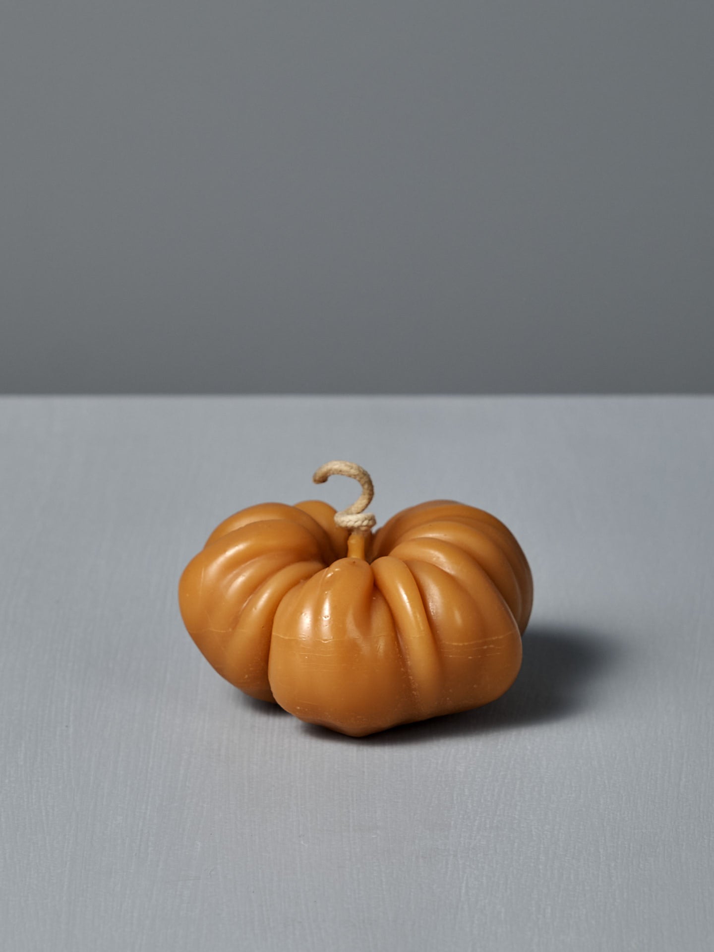 An Orange Heirloom Tomato Candle – Large, featuring a curved wick and handmade design, sits on a light gray surface against a plain gray background.