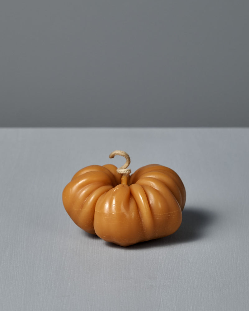An Orange Heirloom Tomato Candle – Large, featuring a curved wick and handmade design, sits on a light gray surface against a plain gray background.