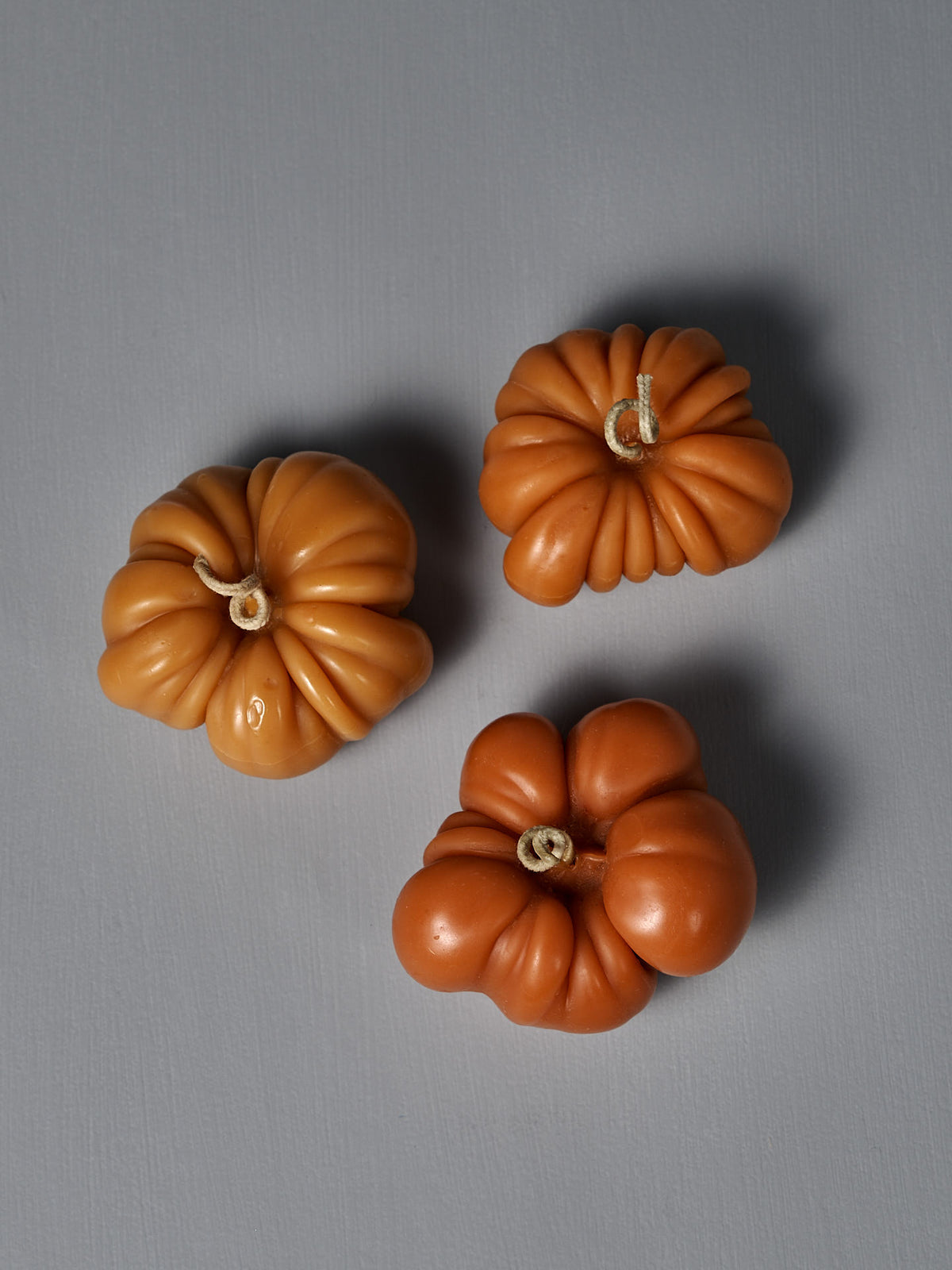 A large, orange, heirloom tomato-shaped candle is displayed on a flat gray surface.