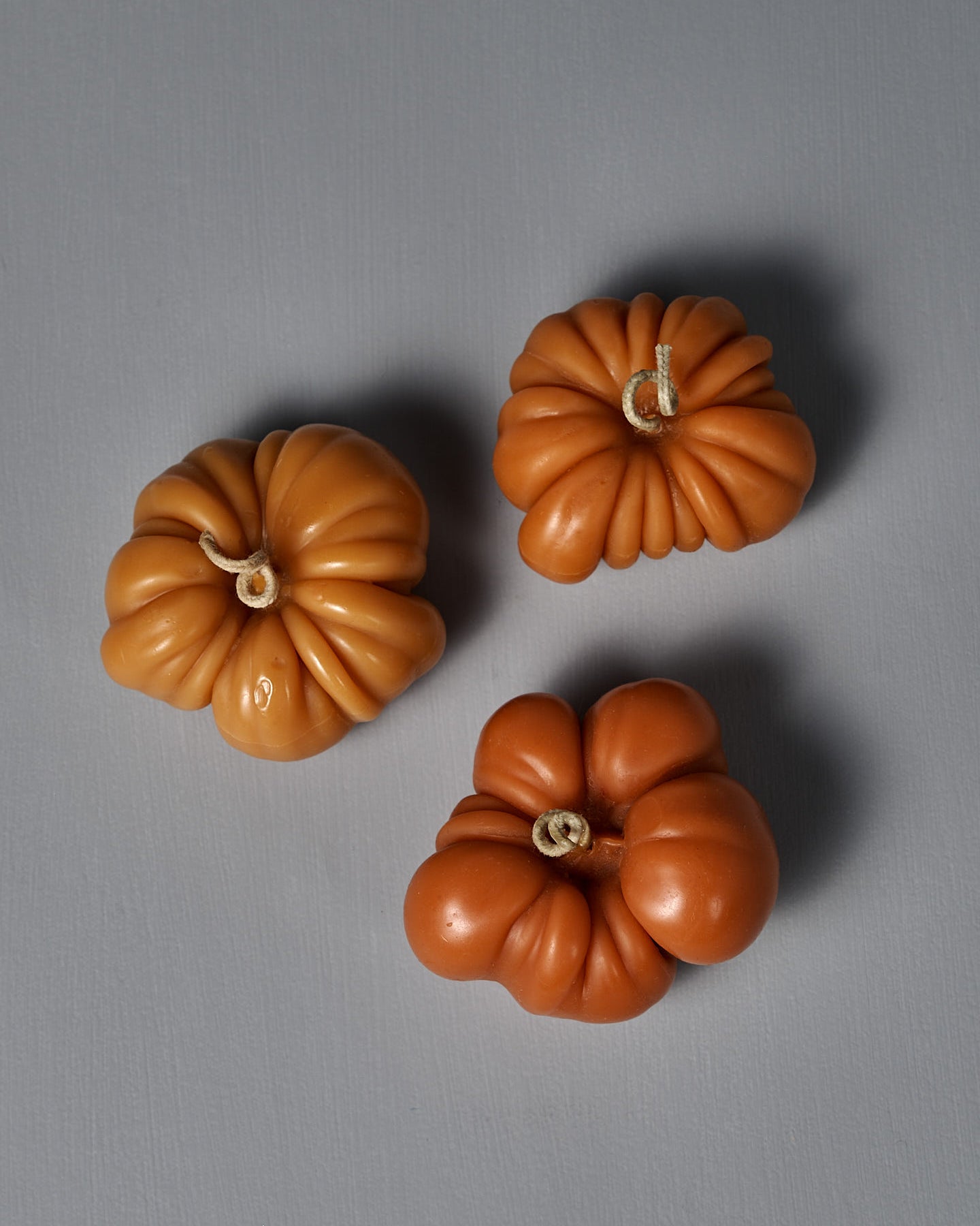 An Orange Heirloom Tomato Candle – Large, featuring a curved wick and handmade design, sits on a light gray surface against a plain gray background.
