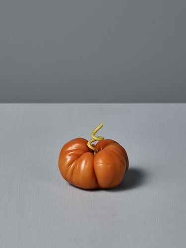The Orange Heirloom Tomato Candle – Small features an irregular shape with a curly green stem, crafted by hand from premium New Zealand beeswax. It’s shown on a gray surface against a gray background.