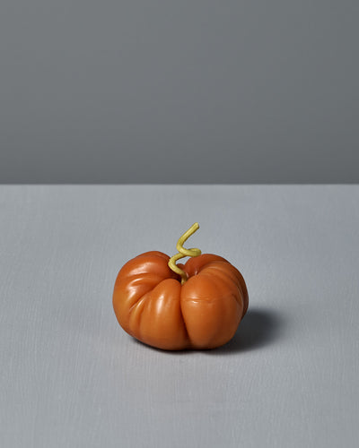 The Orange Heirloom Tomato Candle – Small features an irregular shape with a curly green stem, crafted by hand from premium New Zealand beeswax. It’s shown on a gray surface against a gray background.