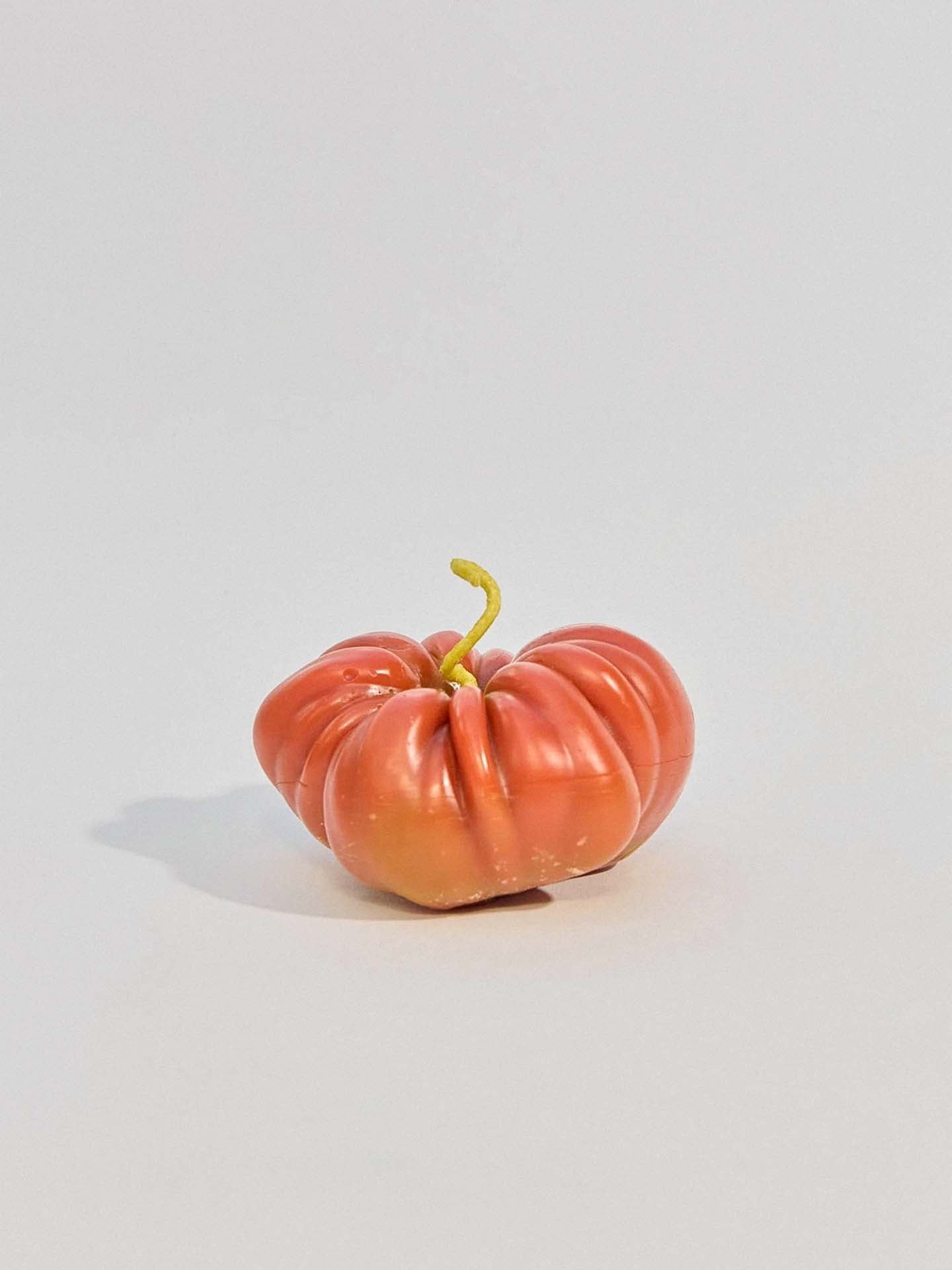 A single, uniquely shaped Orange Heirloom Tomato Candle – Large rests on a light gray surface, its design echoing the natural forms found in New Zealand handmade candles.