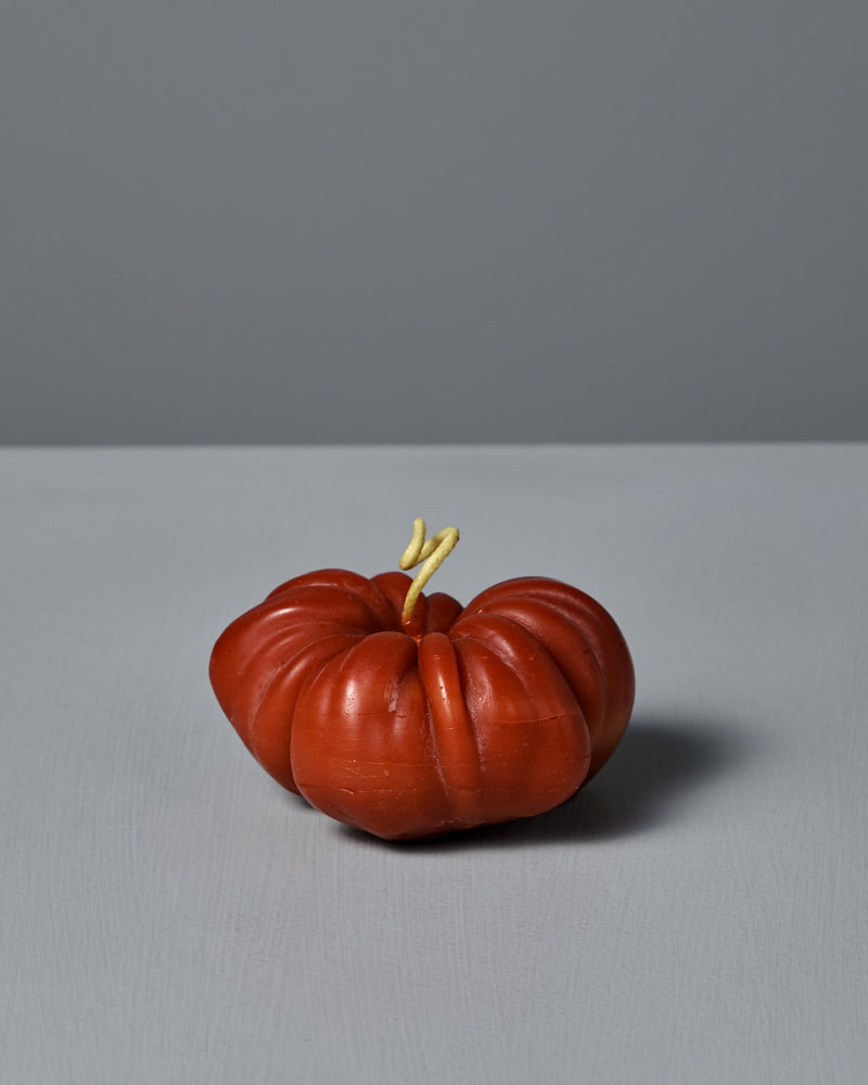 The Red Heirloom Tomato Candle – Small, designed with a realistic misshapen red form and a pale, forked stem, sits on a plain gray surface with a gray background.