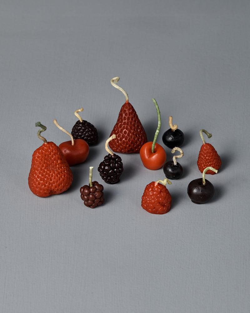 The Mixed Berries Candles – Box of 12 features charming fruit-shaped candles, including strawberries, blackberries, cherries, grapes, and raspberries, crafted from premium New Zealand beeswax and artfully arranged on a gray surface—perfect for adding a unique touch to birthday cake decorations.