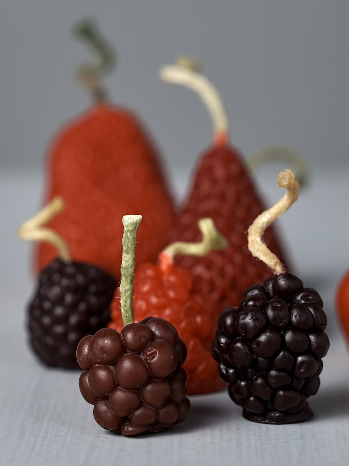 Mixed Berries Candles – Box of 10: Handmade beeswax candles shaped like berries and strawberries with textured surfaces and twisted stems, crafted from New Zealand beeswax and arranged on a light gray surface.