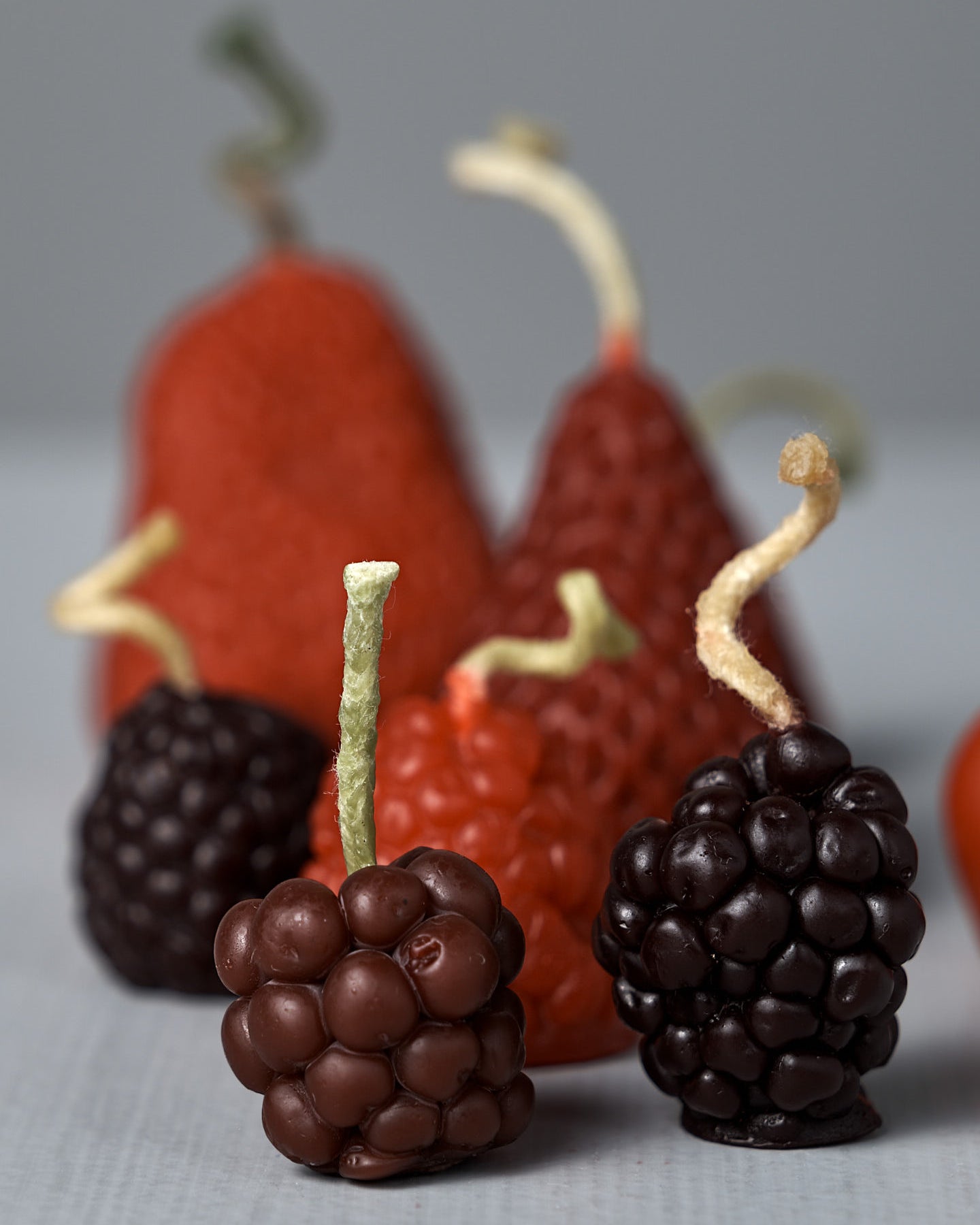 The Mixed Berries Candles – Box of 12 features charming fruit-shaped candles, including strawberries, blackberries, cherries, grapes, and raspberries, crafted from premium New Zealand beeswax and artfully arranged on a gray surface—perfect for adding a unique touch to birthday cake decorations.