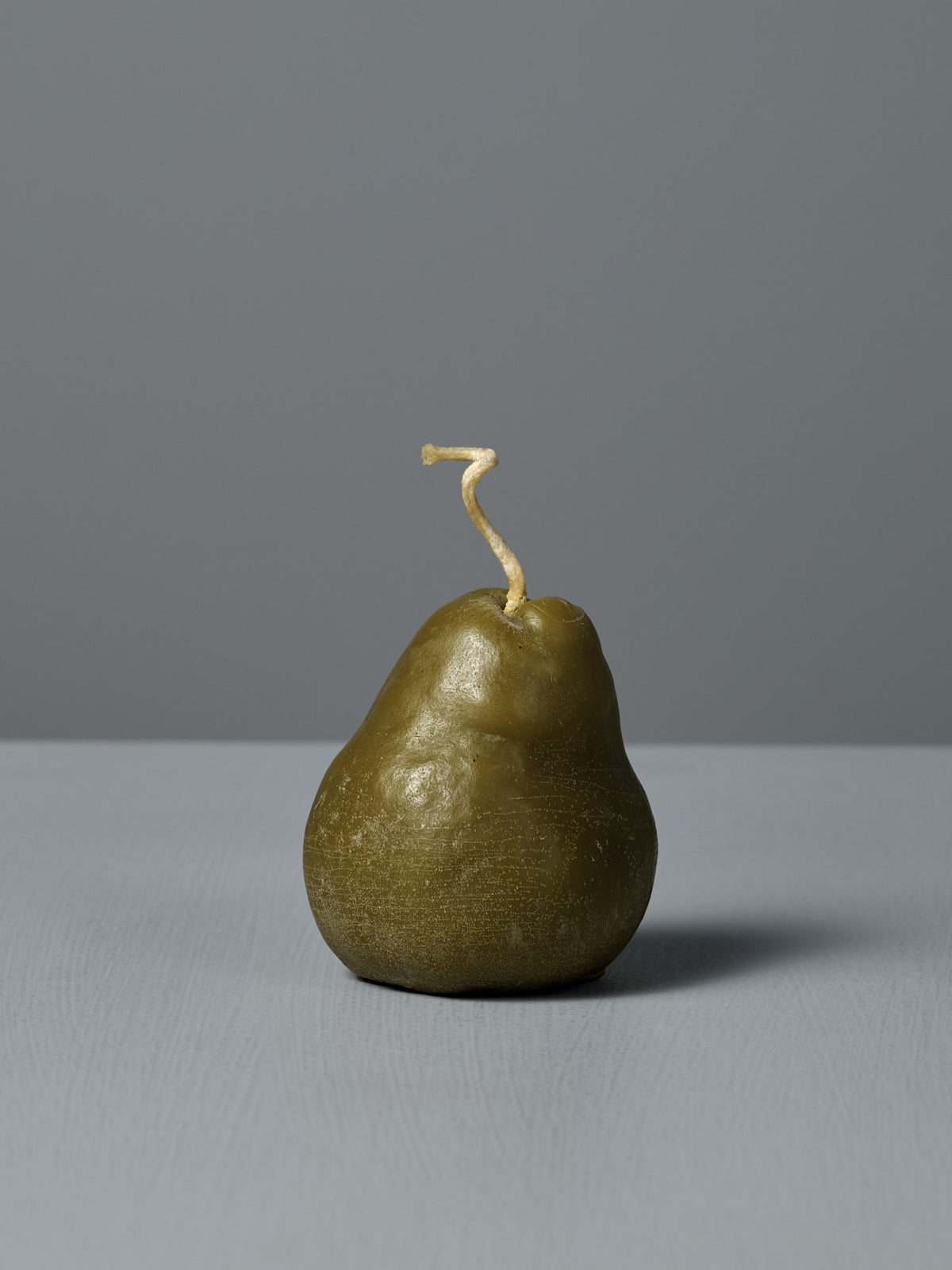 The Green Pear Candle – Large is a handmade, pear-shaped beeswax candle with a curved wick, shown on a gray surface against a gray background—a charming decorative piece.
