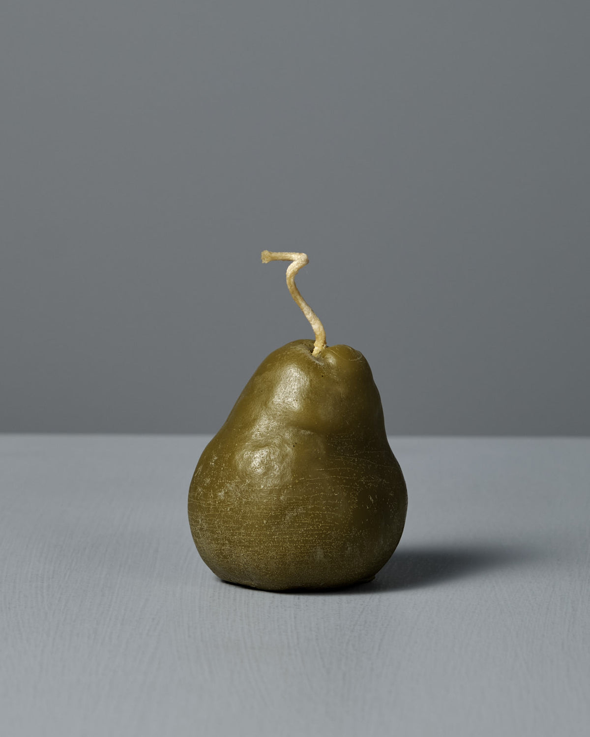 The Green Pear Candle – Large is a handmade, pear-shaped beeswax candle with a curved wick, shown on a gray surface against a gray background—a charming decorative piece.