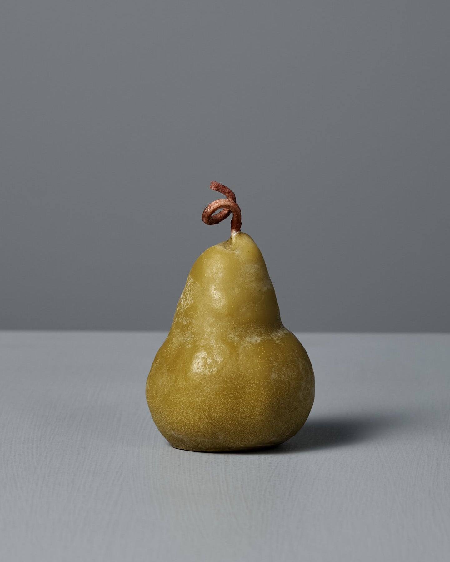 The Green Pear Candle – Large, a handmade pear-shaped candle with a twisted wick, is displayed on a light gray surface against a plain gray background.