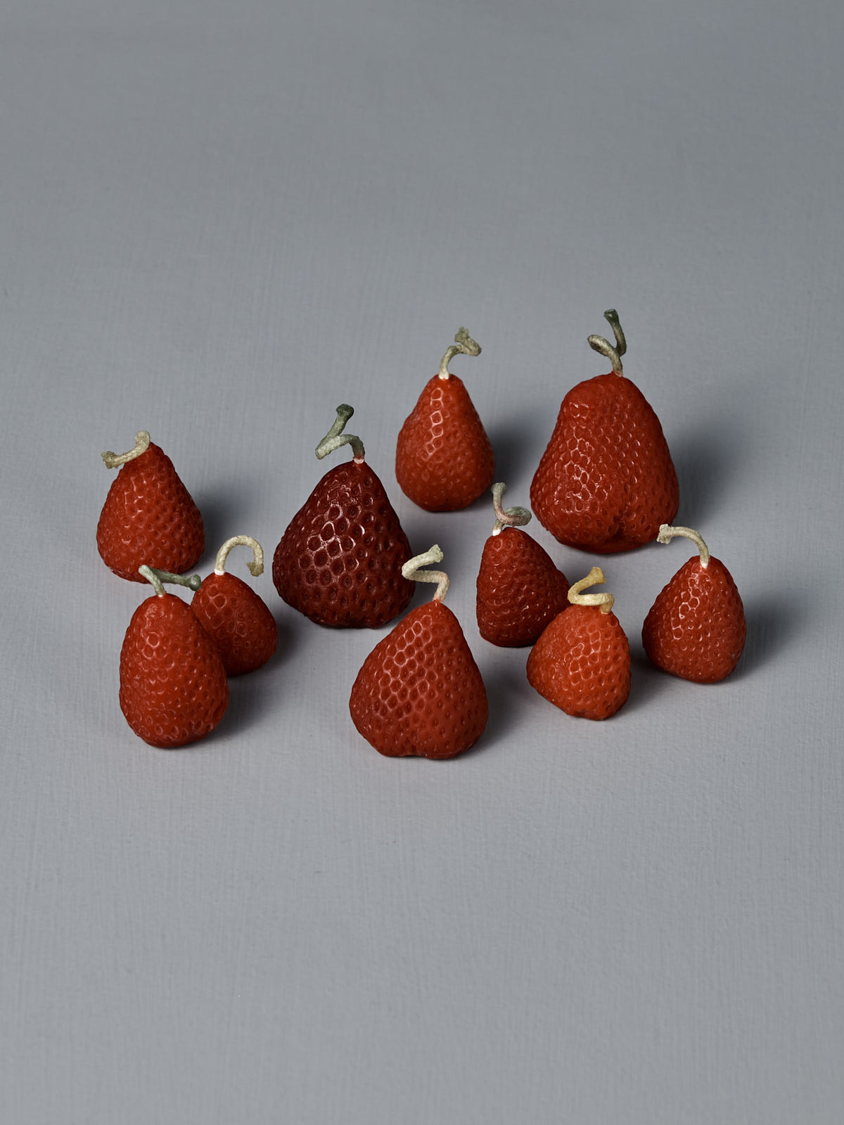 A box of 10 handmade Strawberry Candles, each with a small knotted string on top, is arranged together on a simple light gray surface.