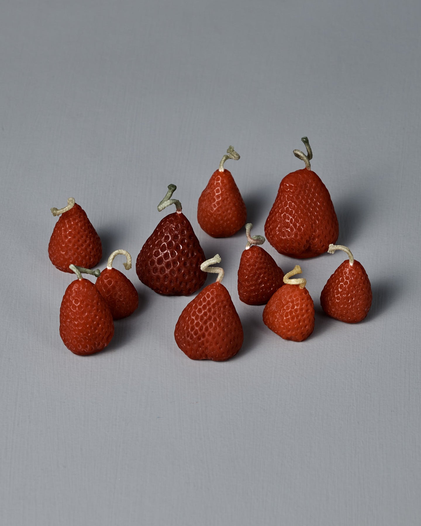 A box of 10 handmade Strawberry Candles, each with a small knotted string on top, is arranged together on a simple light gray surface.