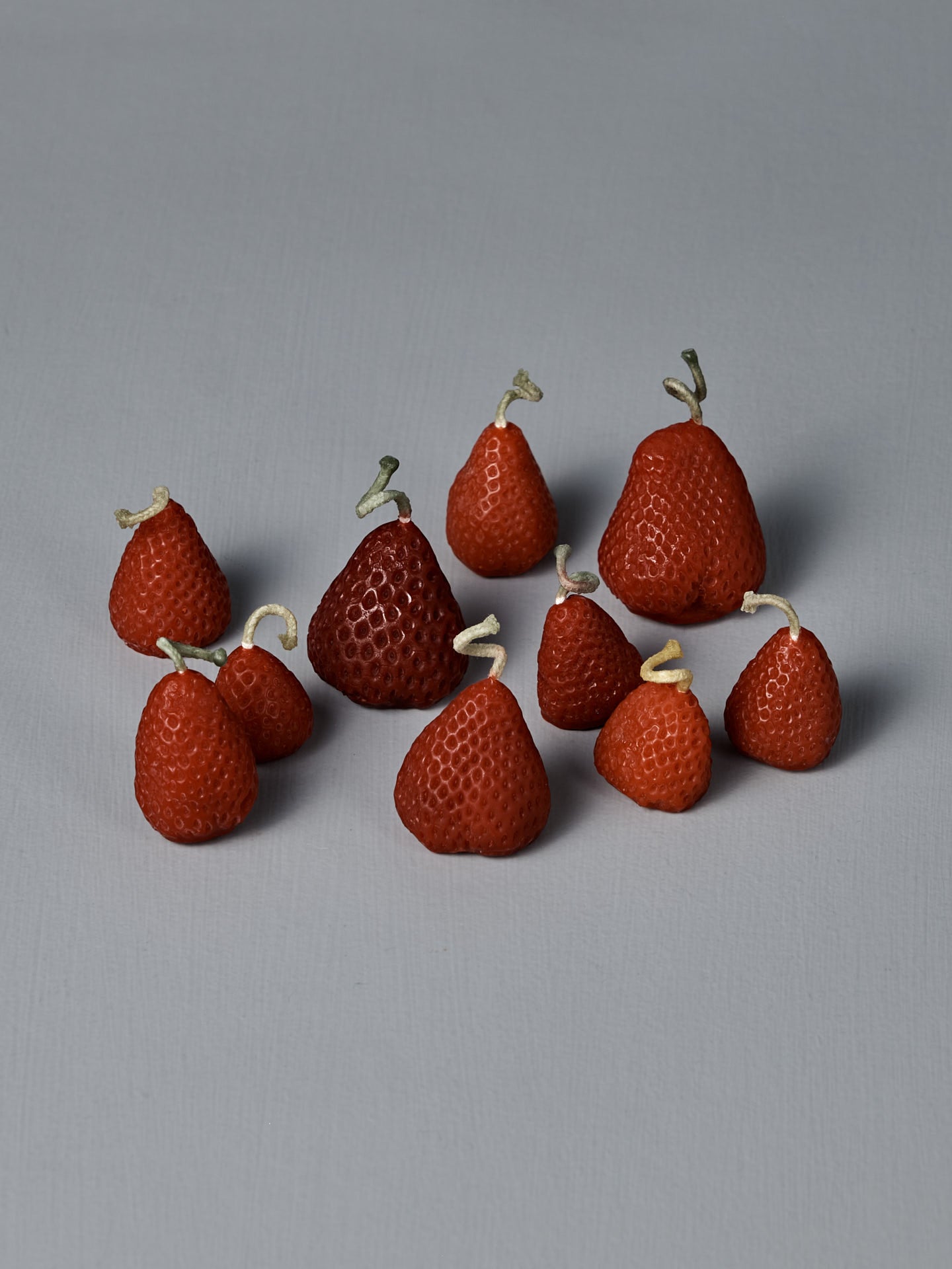 A box of 10 handmade Strawberry Candles, each with a small knotted string on top, is arranged together on a simple light gray surface.