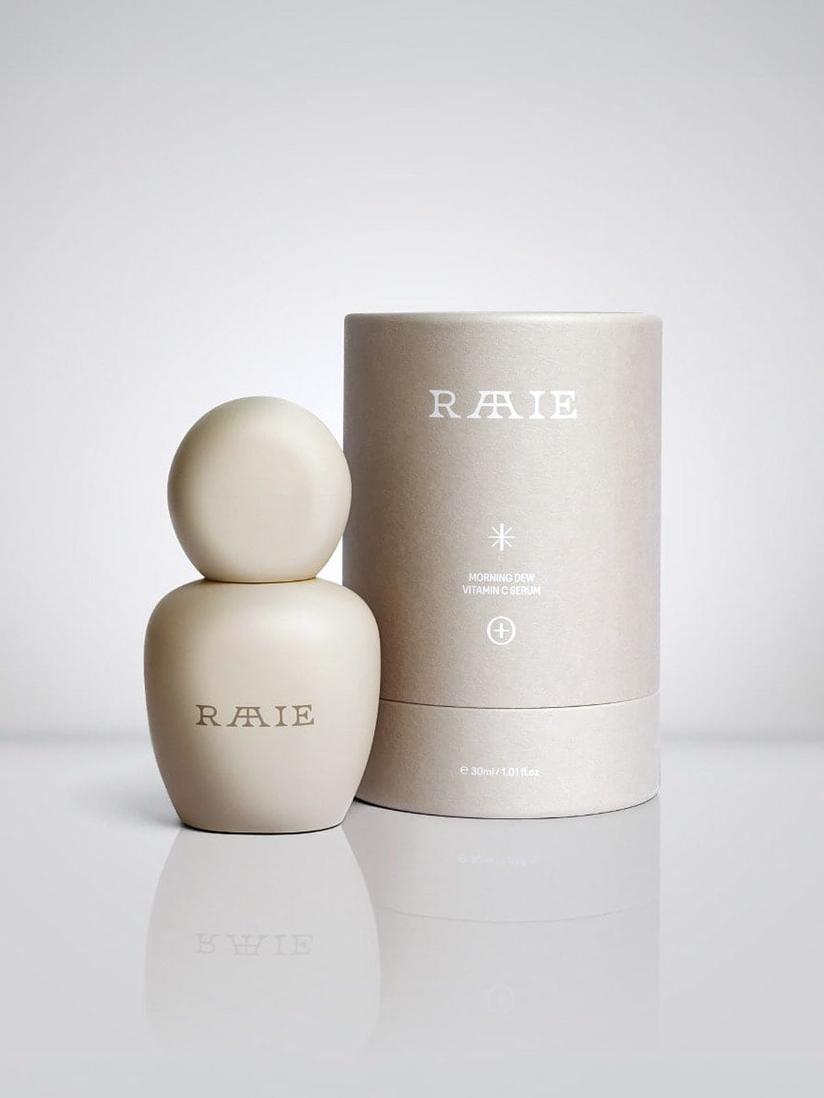 A beige bottle with a rounded cap next to a cylindrical container, both labeled &quot;RAAIE.&quot; The container reads &quot;Morning Dew Vitamin C Serum&quot; and indicates a volume of 30ml/1.01fl oz. Infused with potent New Zealand botanicals, this antioxidant serum revitalizes your skin.