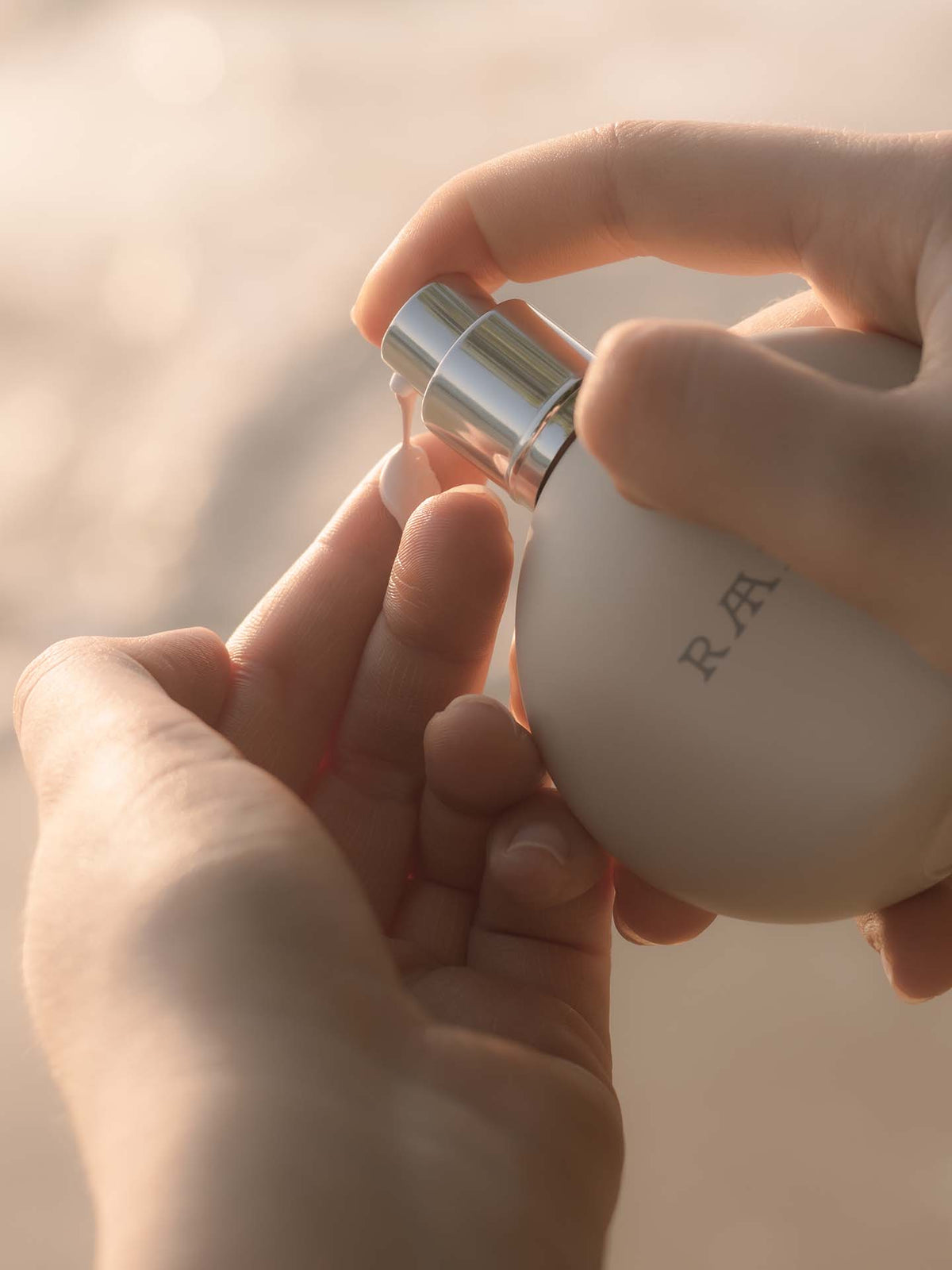 A person pumps a small amount of Sun Milk Drops Tinted SPF 50+ from RAAIE into their hand, enjoying the lightweight formula and mineral sunscreen for broad spectrum protection.