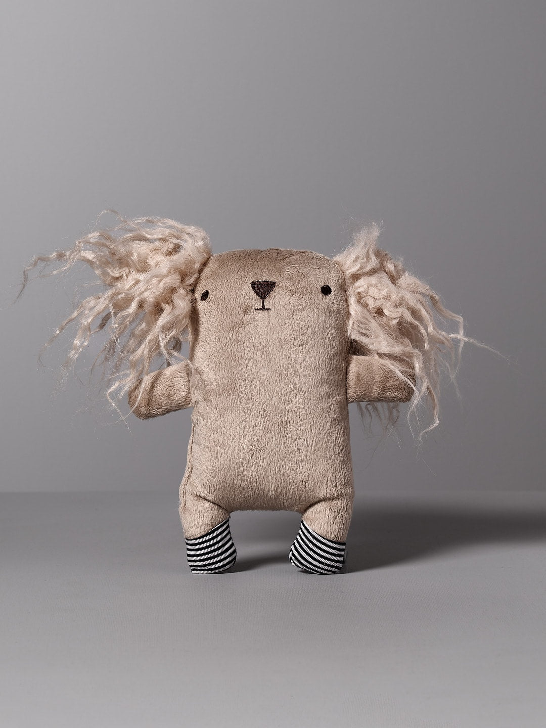 A Raplapla handmade stuffed animal named Léo the Dog with long hair on a grey background.