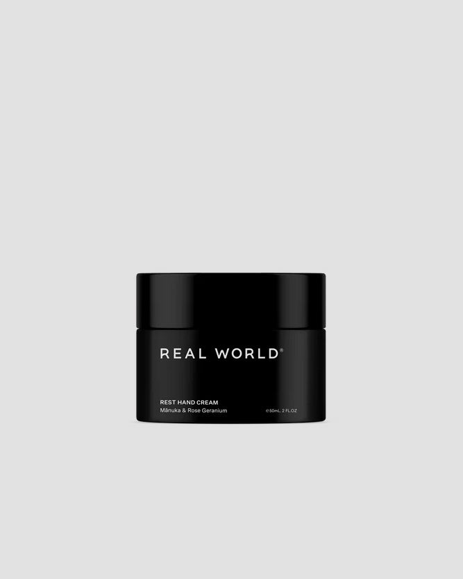 A soothing black jar labeled "Real World" with the keywords Rest Hand Cream – Mānuka & Rose Geranium.