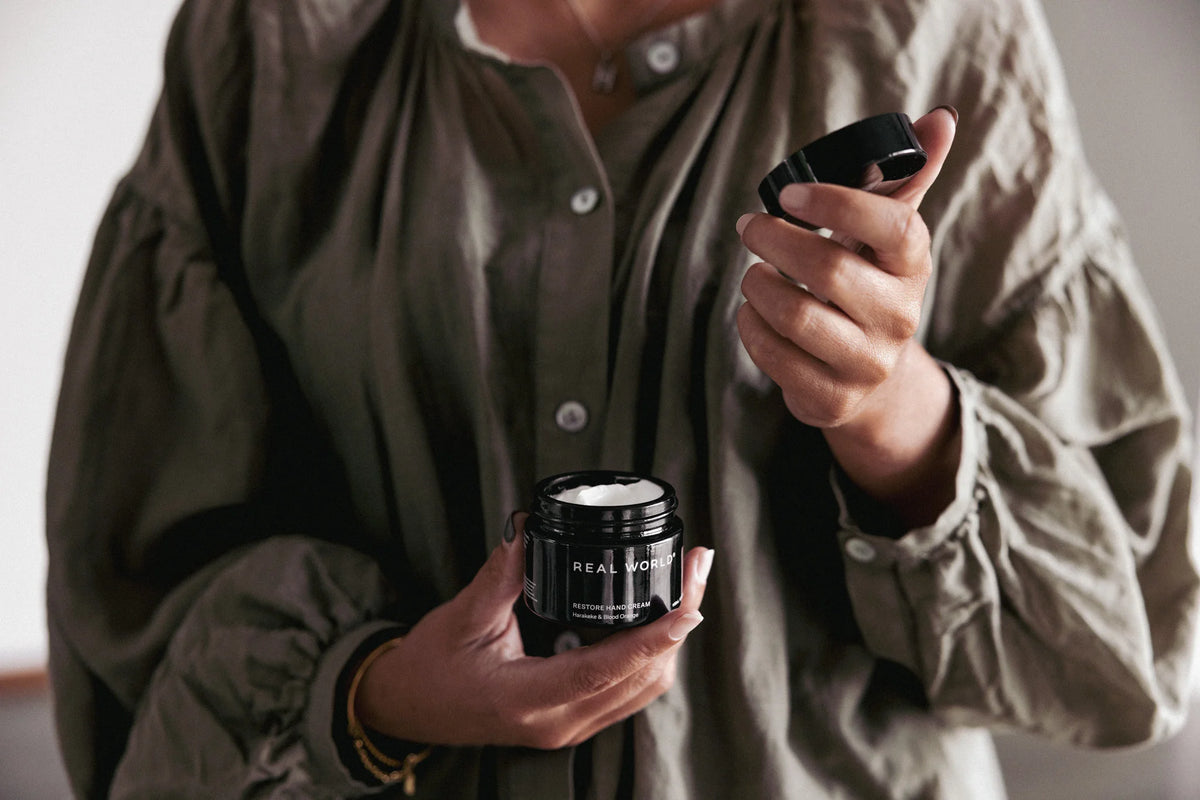 A woman holding a jar of Rest Hand Cream – Mānuka &amp; Rose Geranium with Real World.