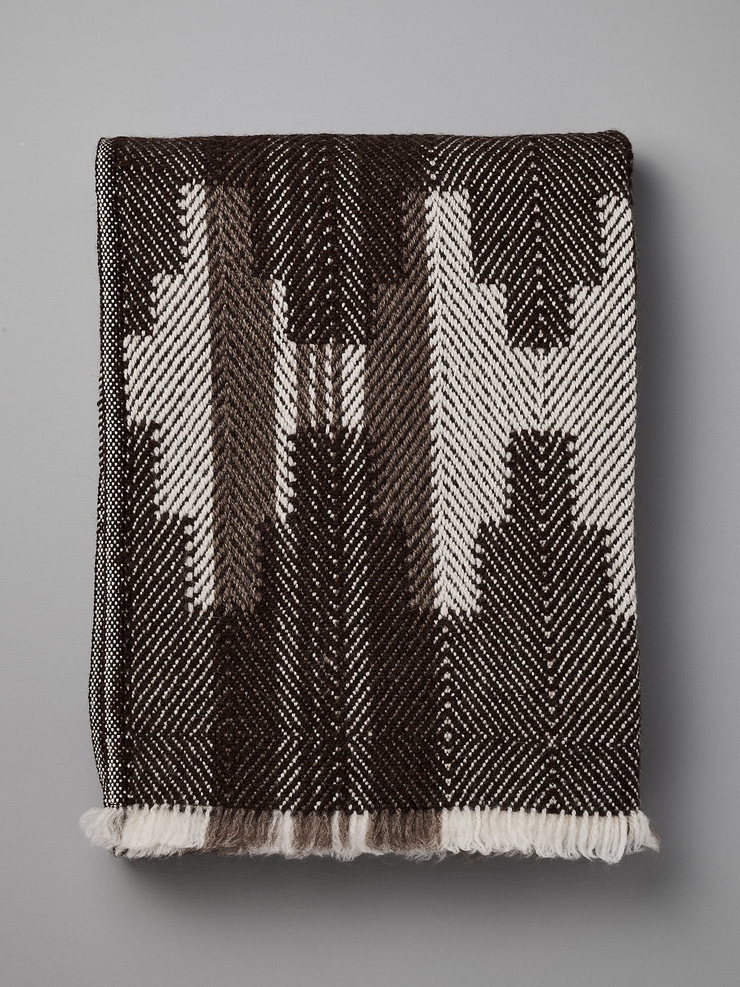 A folded, black and white patterned blanket with geometric designs, reminiscent of traditional Bulgarian shevitza, is displayed against a plain gray background. 

Replace with: 

A folded Rodopska Takan "Bulgarian Shevitza Wool Blanket – Brown" with geometric designs, reminiscent of traditional Bulgarian shevitza, is displayed against a plain gray background.