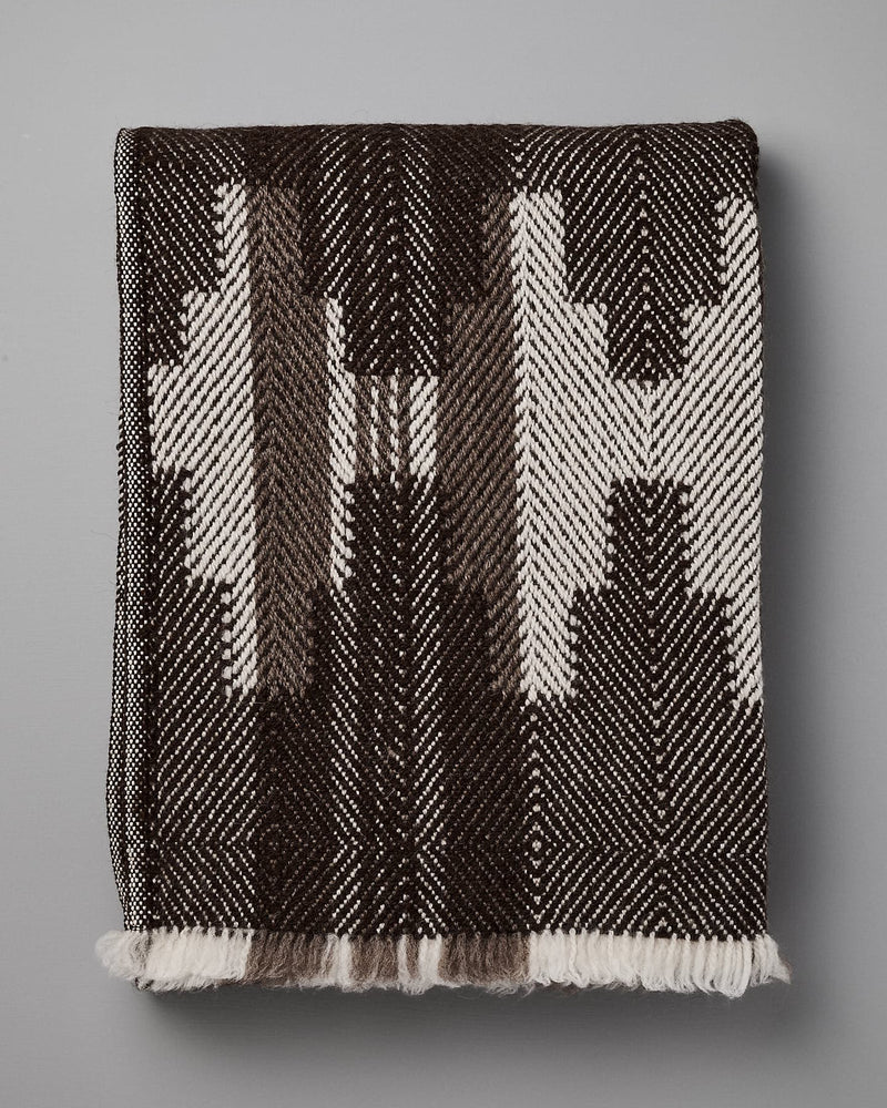A folded, black and white patterned blanket with geometric designs, reminiscent of traditional Bulgarian shevitza, is displayed against a plain gray background. 

Replace with: 

A folded Rodopska Takan "Bulgarian Shevitza Wool Blanket – Brown" with geometric designs, reminiscent of traditional Bulgarian shevitza, is displayed against a plain gray background.