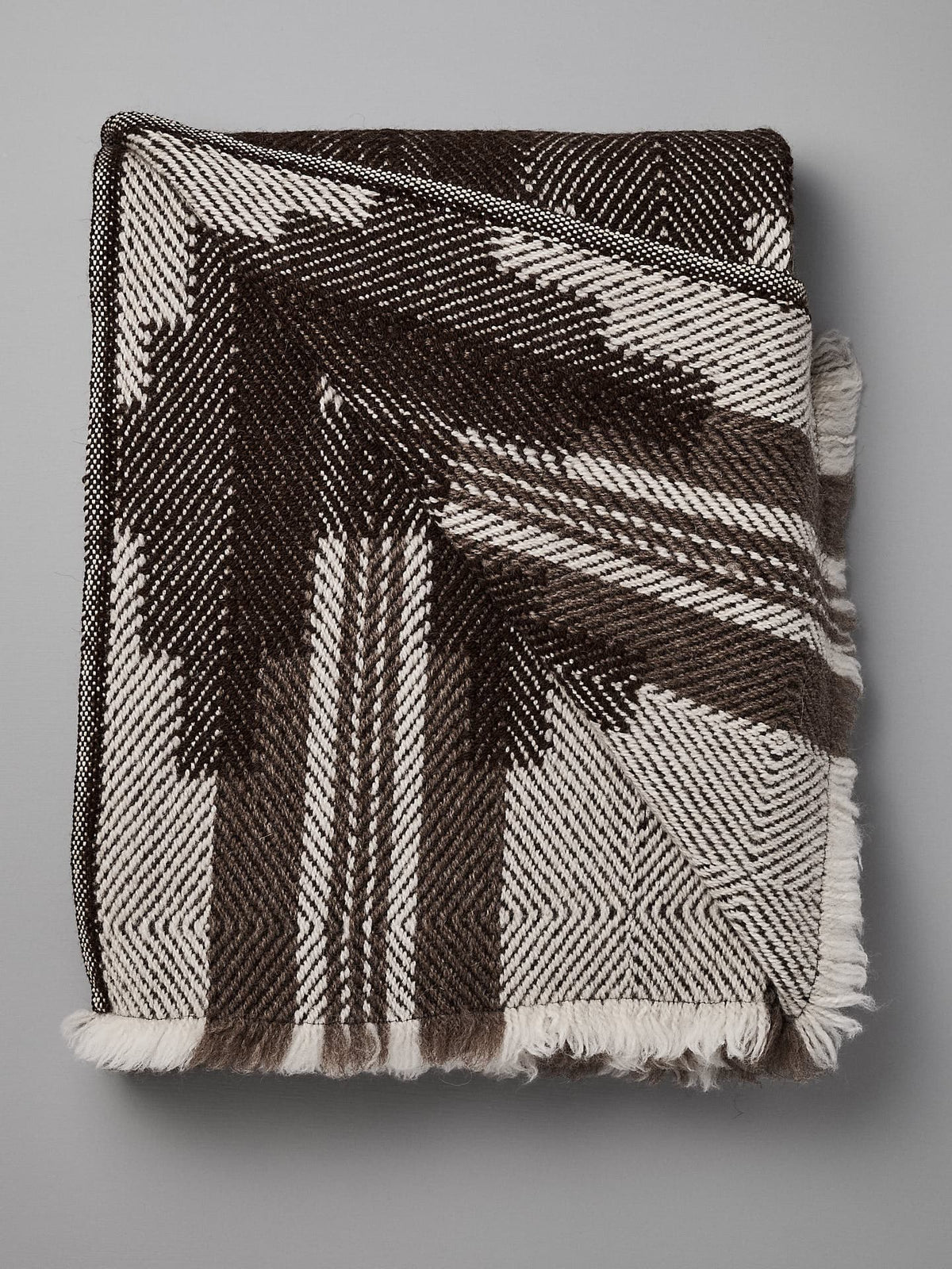 A folded **Rodopska Takan Bulgarian Shevitza Wool Blanket – Brown** with a geometric black and white pattern, crafted from locally sourced wool. The blanket has fringed edges and offers the heavy, warm comfort perfect for winter.