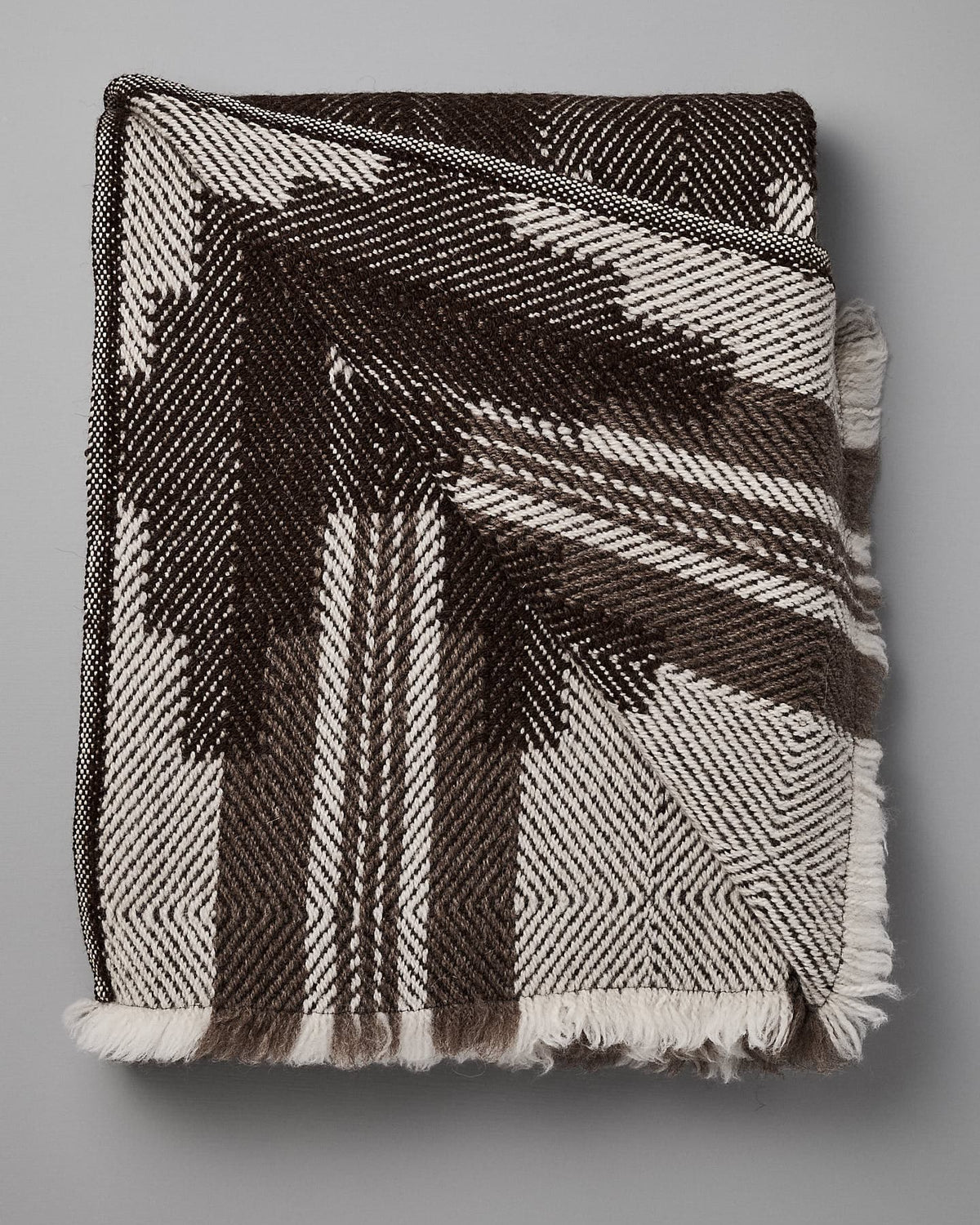 A folded **Rodopska Takan Bulgarian Shevitza Wool Blanket – Brown** with a geometric black and white pattern, crafted from locally sourced wool. The blanket has fringed edges and offers the heavy, warm comfort perfect for winter.