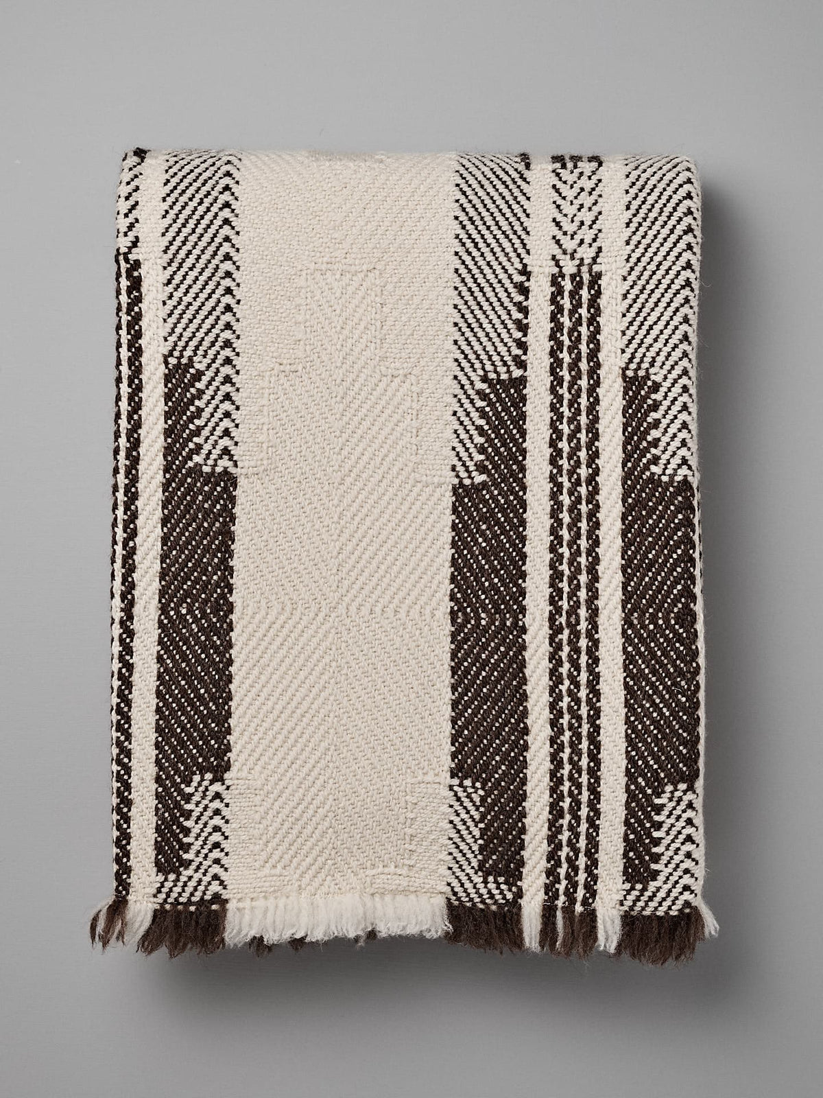 Rolled-up woven traditional wool blanket, the Bulgarian Shevitza Wool Blanket – Cream by Rodopska Takan, with a geometric pattern, predominantly in beige and brown colors, lying on a gray surface.