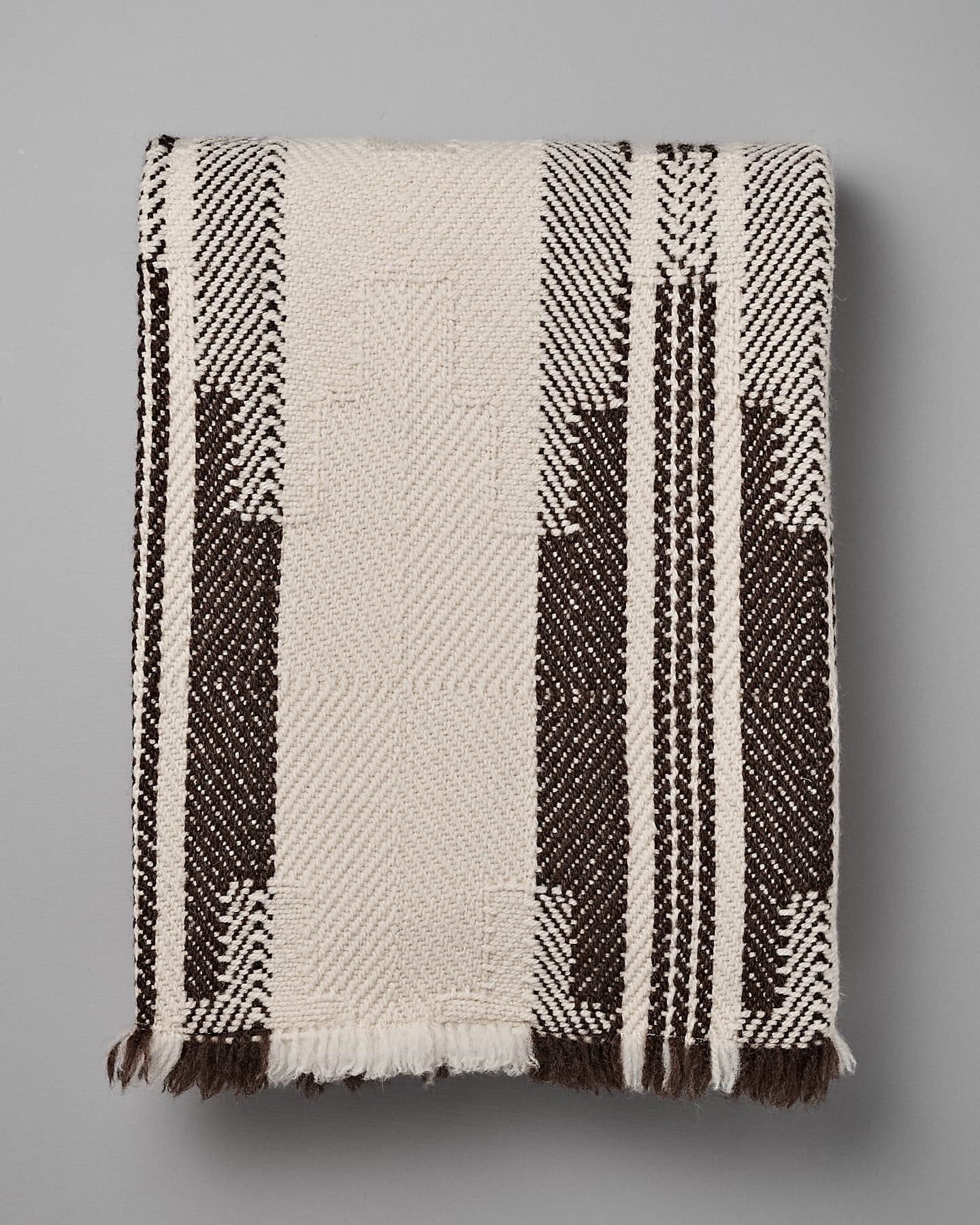 Rolled-up woven traditional wool blanket, the Bulgarian Shevitza Wool Blanket – Cream by Rodopska Takan, with a geometric pattern, predominantly in beige and brown colors, lying on a gray surface.