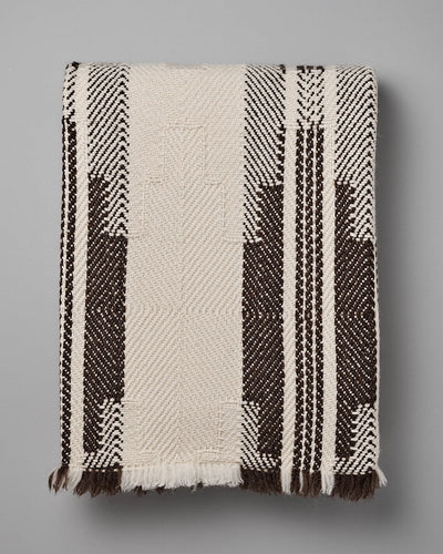 Rolled-up woven traditional wool blanket, the Bulgarian Shevitza Wool Blanket – Cream by Rodopska Takan, with a geometric pattern, predominantly in beige and brown colors, lying on a gray surface.
