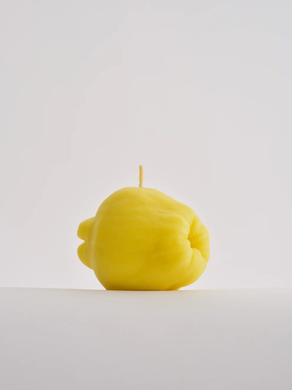 A hand-finished yellow Nonna&#39;s Grocer Quince Candle, made from a soy wax blend, sitting on a white surface.