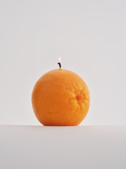 A handmade Nonna&#39;s Grocer Orange Candle gracefully illuminates a white surface.
