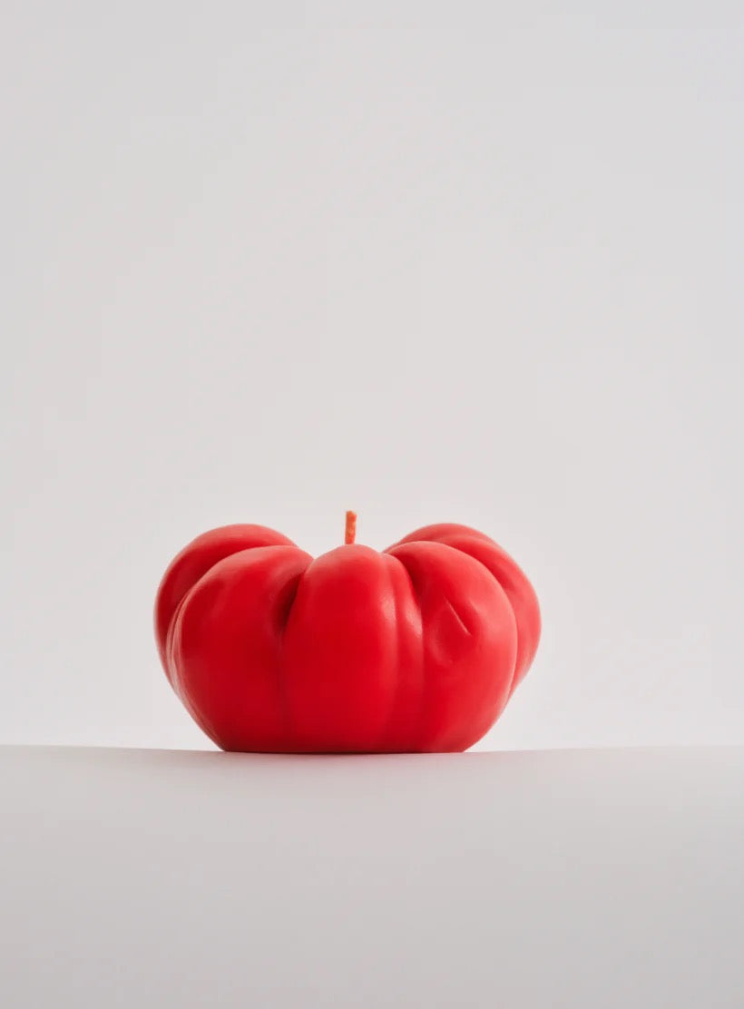A large Tomato Candle from Nonna's Grocer, made from a soy wax blend, sits on top of a white surface.