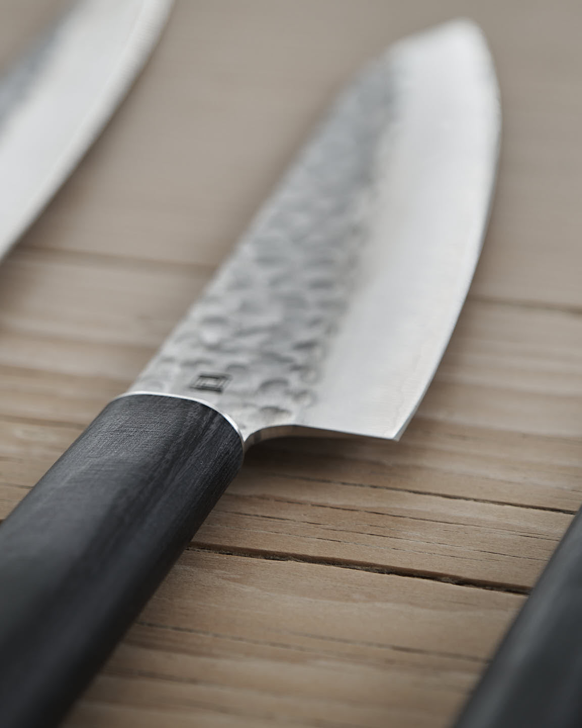 A Shizu Hamono Co. Yamato Yanagiba Knife with a black handle rests atop a wooden box adorned with a geometric logo on a light gray surface.