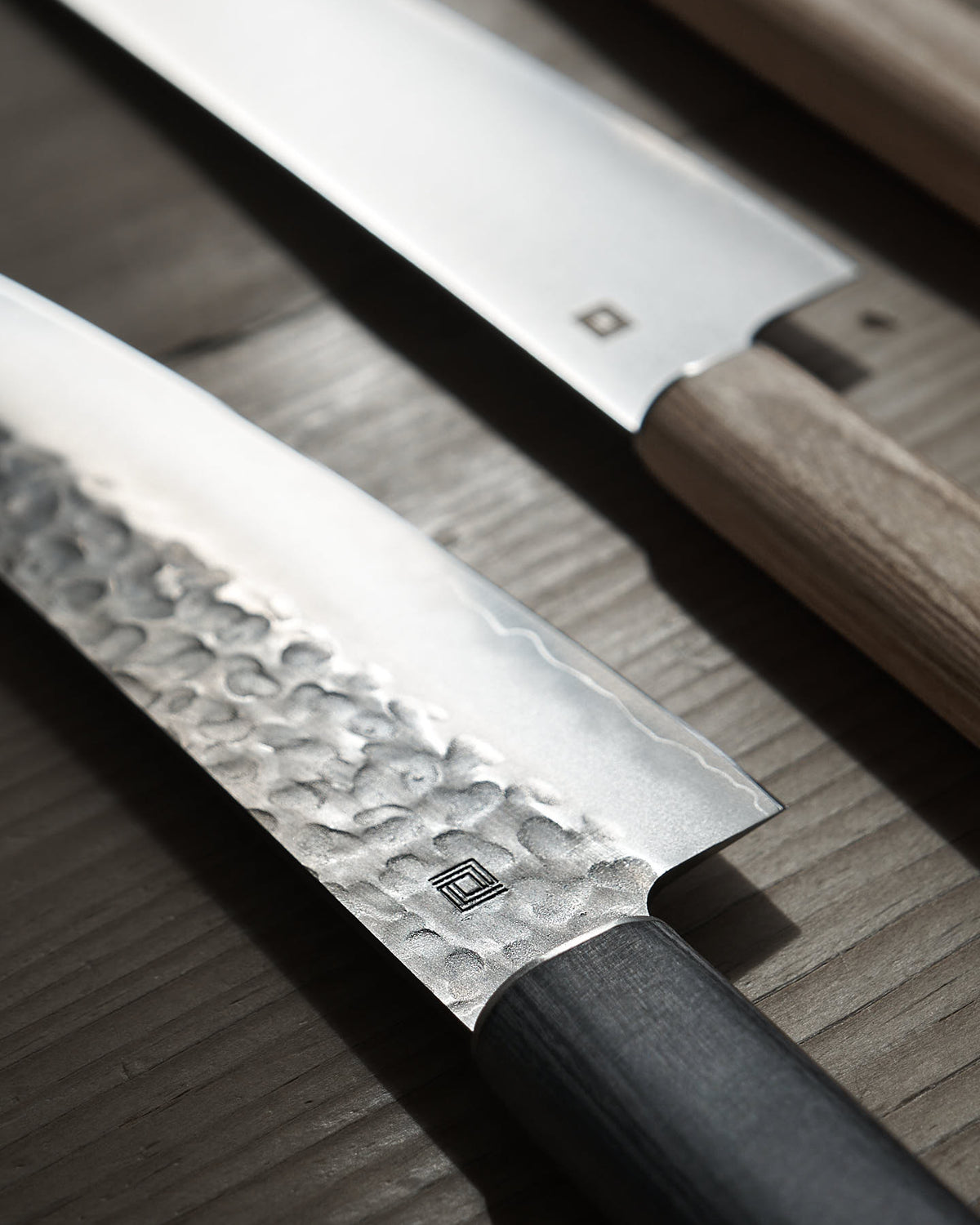 Close-up of two Yamato Deba Knives by Shizu Hamono Co., featuring textured Sanmai steel blades and wooden handles, showcasing traditional Japanese design on a wooden surface.