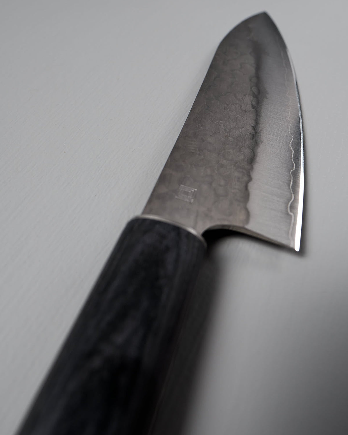 Close-up of a Shizu Hamono Co. Yamato Deba Knife with a black handle on a light grey surface. The Japanese knife features a distinctive hammered texture on its blade.