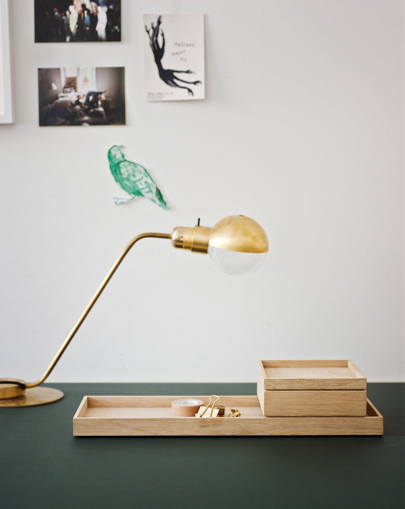 A desk with a brass table lamp, a wooden organizer with compartments, and a few decorative images on a white wall in the background.