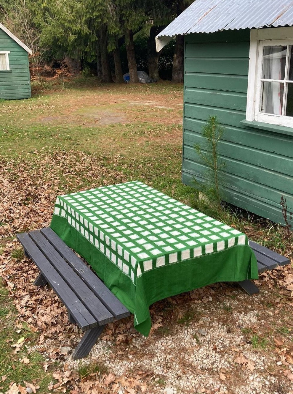 A picnic table with a handwoven, green and white Ikat Weave Tablecloth – Green Grid tablecloth from Stitchwallah.