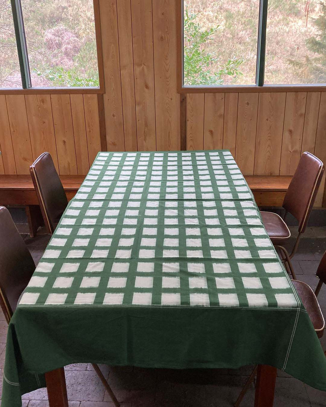 A handwoven Stitchwallah Ikat Weave Tablecloth – Green Grid, beautifully drapes across a wooden table.