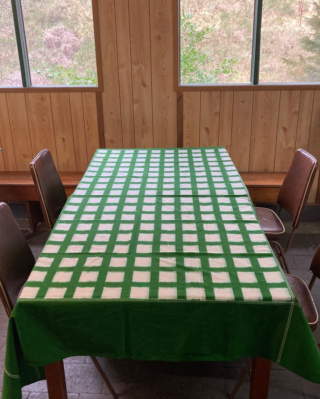A handwoven Stitchwallah Ikat Weave Tablecloth – Green Grid, beautifully drapes across a wooden table.