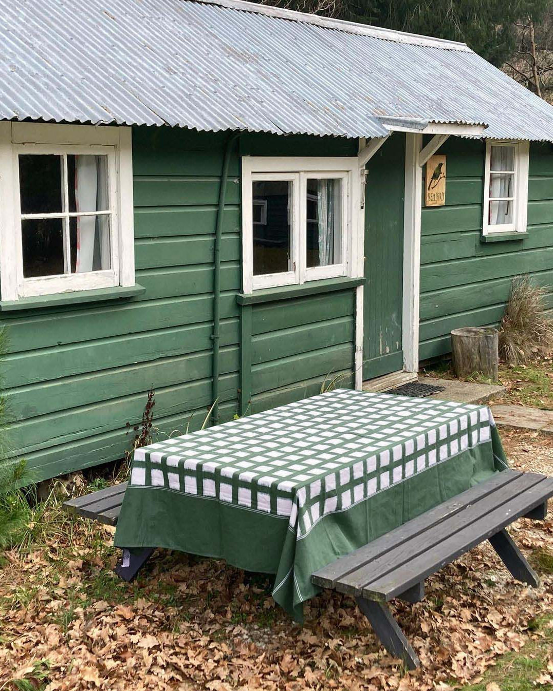 A handwoven green cabin with a picnic table and Stitchwallah Ikat Weave Tablecloth – Green Grid made of dyed yarns.