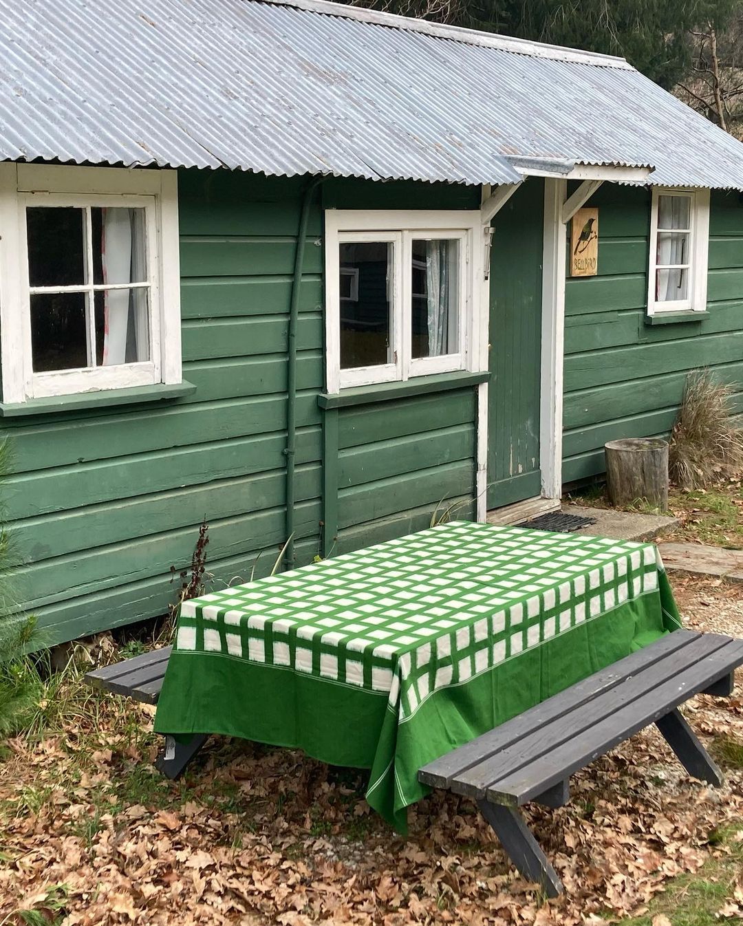 A handwoven green cabin with a picnic table and Stitchwallah Ikat Weave Tablecloth – Green Grid made of dyed yarns.