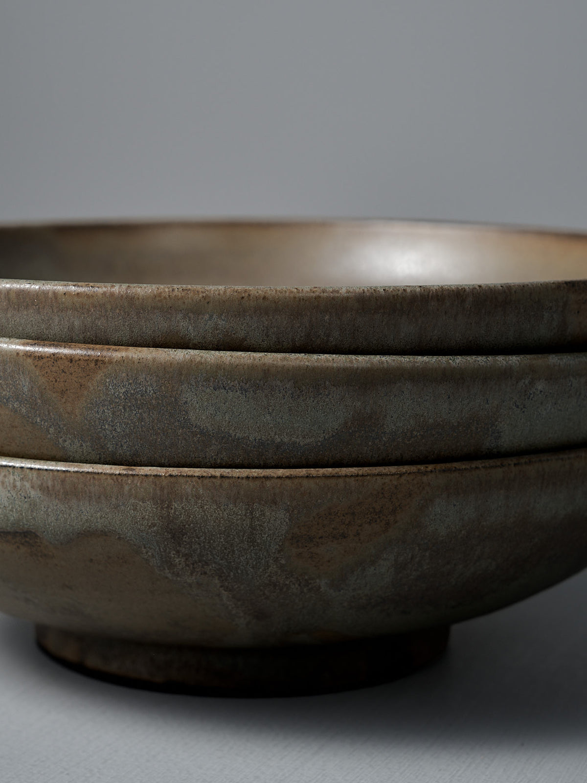 Two Shallow Serving Bowls – Raw Umber, featuring a matte earthy brown finish, are stacked against a plain gray background, highlighting the handmade craftsmanship of Studio Foon.