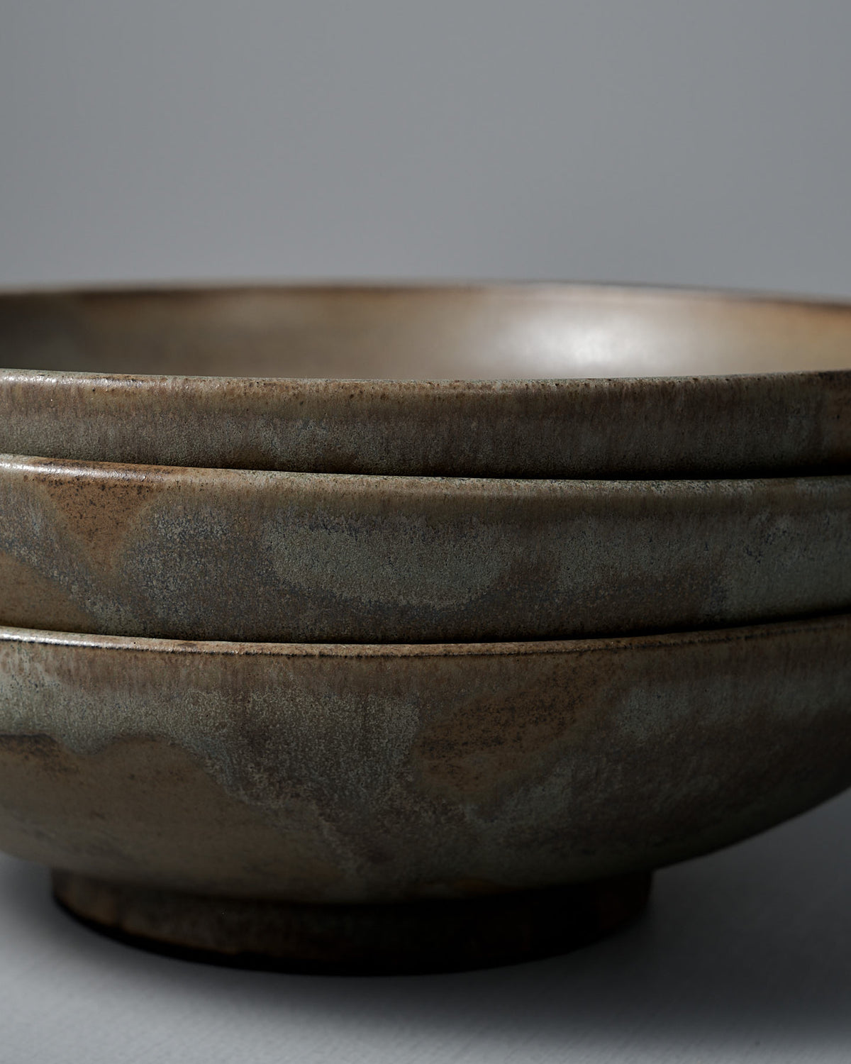 Two Shallow Serving Bowls – Raw Umber, featuring a matte earthy brown finish, are stacked against a plain gray background, highlighting the handmade craftsmanship of Studio Foon.