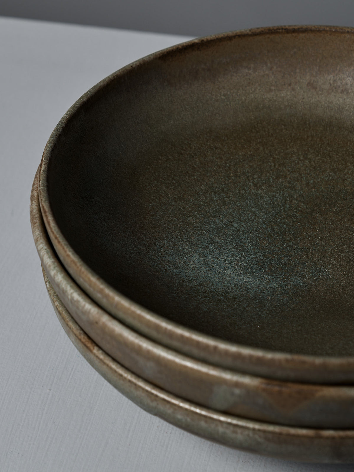 Close-up of three Shallow Serving Bowls – Raw Umber, handmade with a matte, textured finish on a light gray background—crafted by Studio Foon, perfect for serving.