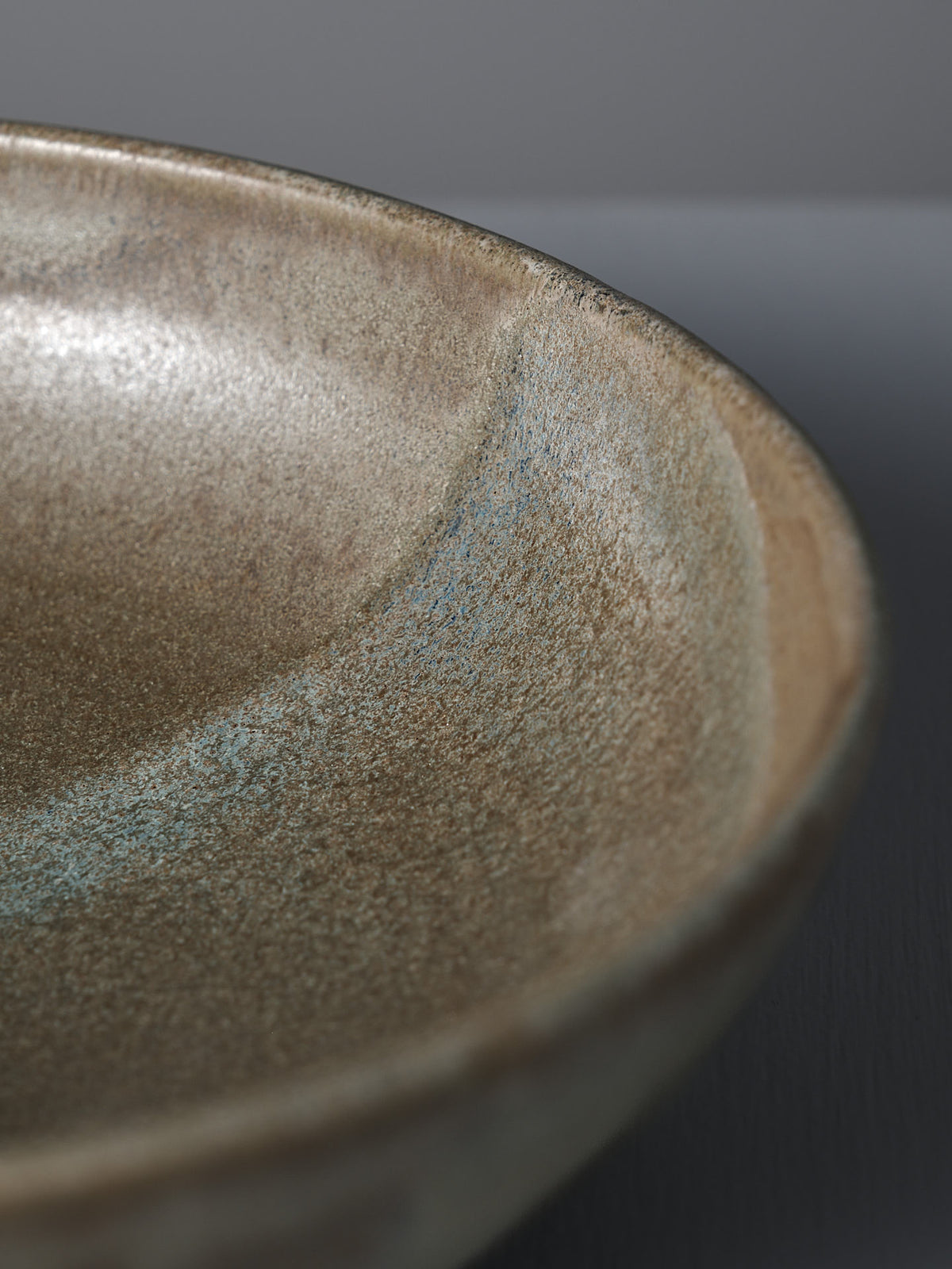 Close-up of the Shallow Serving Bowl – Raw Umber by Studio Foon, featuring earthy tones, a curved edge, and a textured matte finish.