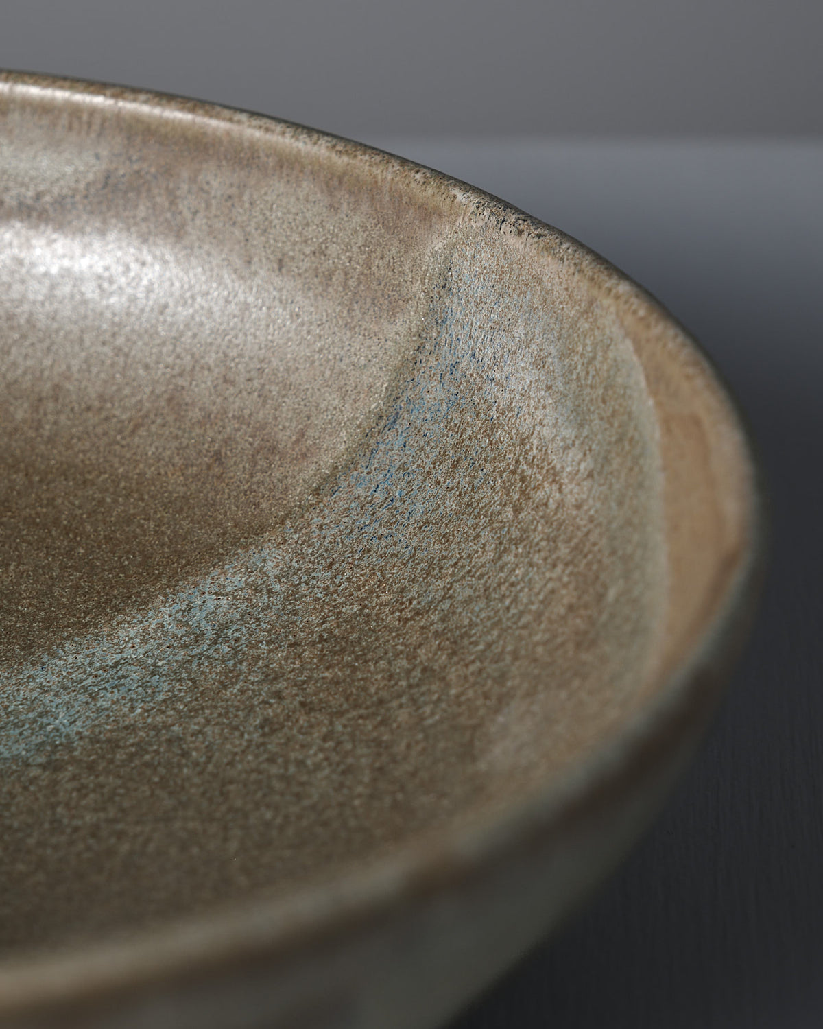 Close-up of the Shallow Serving Bowl – Raw Umber by Studio Foon, featuring earthy tones, a curved edge, and a textured matte finish.