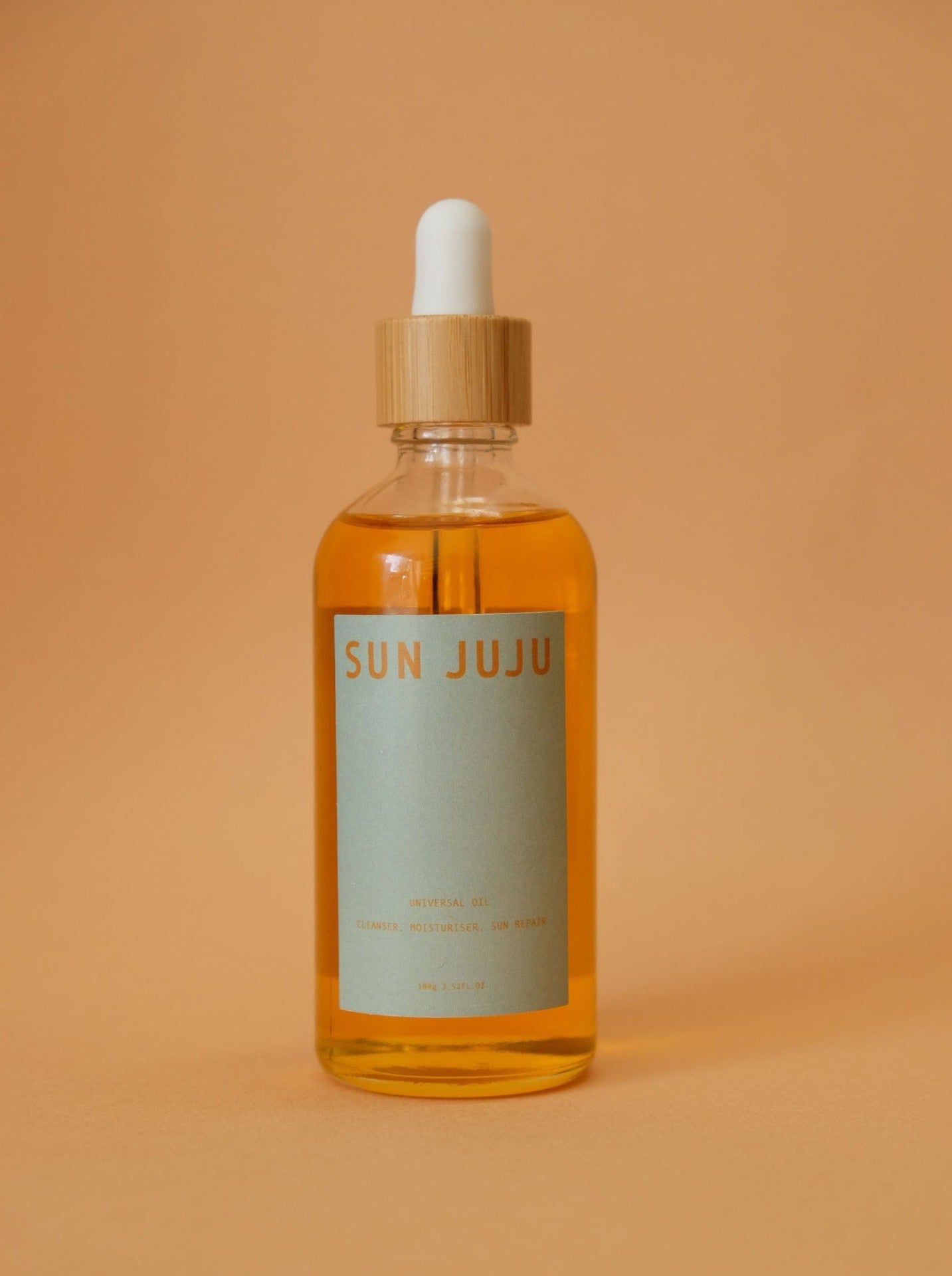 A bottle of Sun Juju Universal Oil – 100𝚐 on an orange background, promising to heal and hydrate.